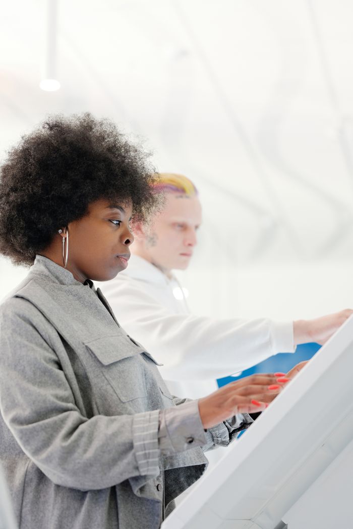 Side view of a fashionable woman with afro hair using a touchscreen indoors.